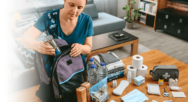 Person preparing an emergency kit with food, water, and first aid supplies