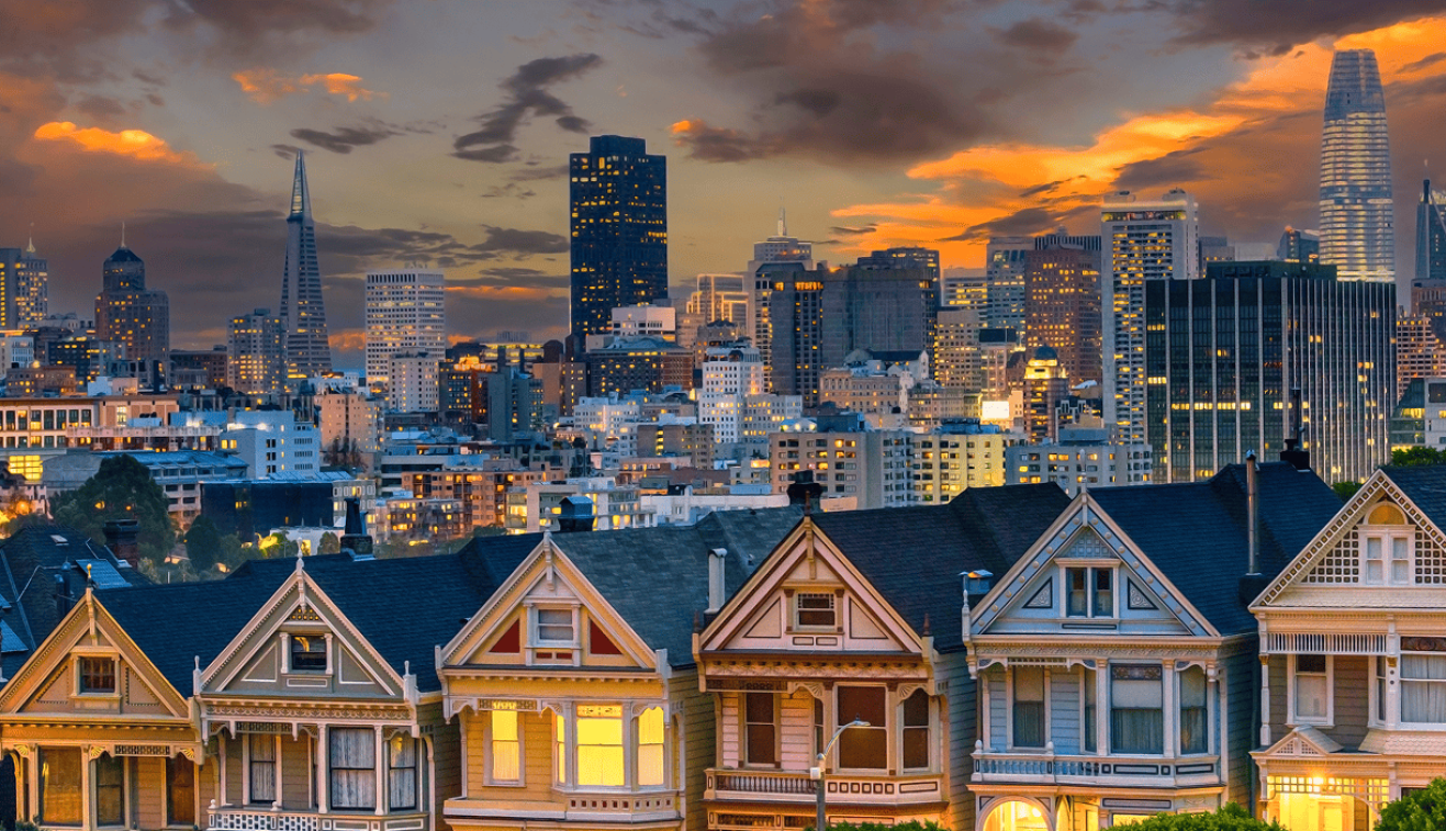 Colorful houses in front of a city skyline at sunset